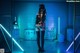 A woman in a black outfit holding a gun in a dark room.