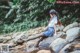 A woman sitting on a rock in a stream.