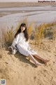 A woman in a white dress sitting on a sandy beach.