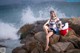 A woman sitting on a rock by the ocean.