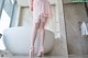 A woman in a pink robe and high heels standing in a bathroom.