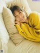 A woman laying on a bed with a yellow sweater on.