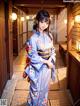 A woman in a blue kimono standing in a hallway.